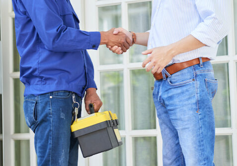 Man thanks the repairman for the good work and shaking hands with him opposite the door of his house